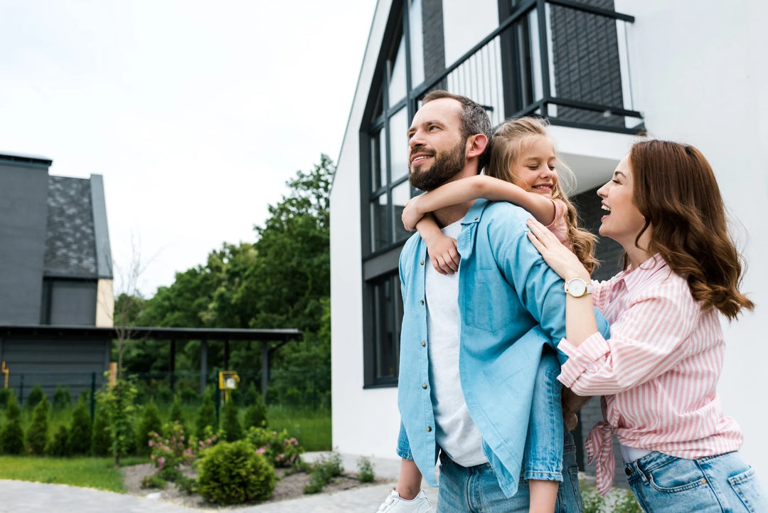 Glückliche Familie vor ihrem renovierten Haus mit frisch gestrichener weißer Fassade - Ergebnis professioneller Fassadengestaltung