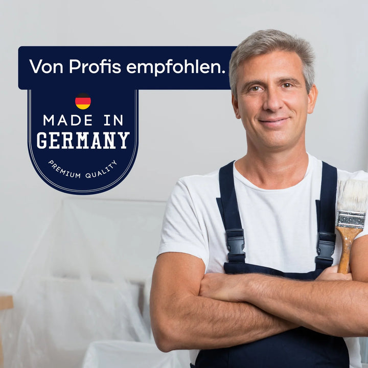 Ein lächelnder Mann in einem Arbeitsoverall hält einen Pinsel und steht neben einem Schild mit der Aufschrift "Von Profis empfohlen. Made in Germany. Premium Quality" mit einer deutschen Flagge - ideal für plid Holzschutzlasur außen wetterfest &amp; atmungsaktiv in vorbereiteten Räumen.