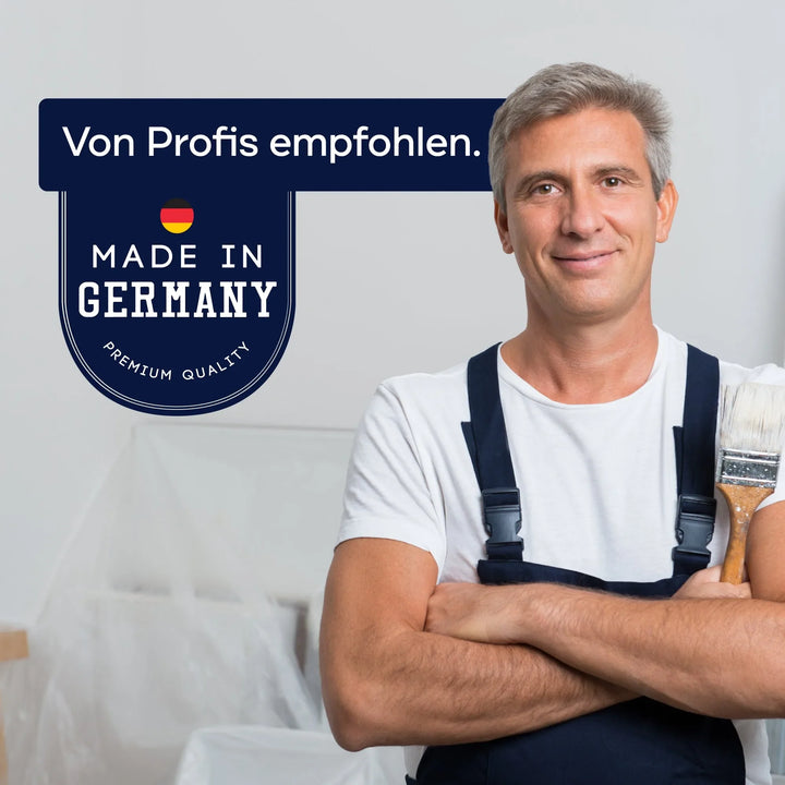 Ein lächelnder Mann in einem Arbeitsoverall hält einen Pinsel und steht in einem Reinraum. Auf einem Schild steht: Von Profis empfohlen. Made in Germany - Premium Quality plid Holzlasur - Anstreichset mit Deutschlandflagge, ideal für wetterfesten Holzschutz.