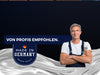 Ein lächelnder Mann im Arbeitsanzug steht mit verschränkten Armen. Der Text lautet VON PROFIS EMPFOHLEN und MADE IN GERMANY PREMIUM QUALITY mit einer kleinen deutschen Flagge auf einem gewellten silbernen Hintergrund.