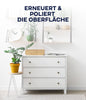 Eine schlichte weiße Kommode mit drei Schubladen steht an einer weißen Wand, die mit Pflanzen geschmückt ist. Auf den Regalen darüber befinden sich weitere Grünpflanzen, eine Uhr und Dekoration. Der fettgedruckte deutsche Text lautet: ERNEUERT & POLIERT DIE OBERFLÄCHE-plid Möbellack - Lackierset.